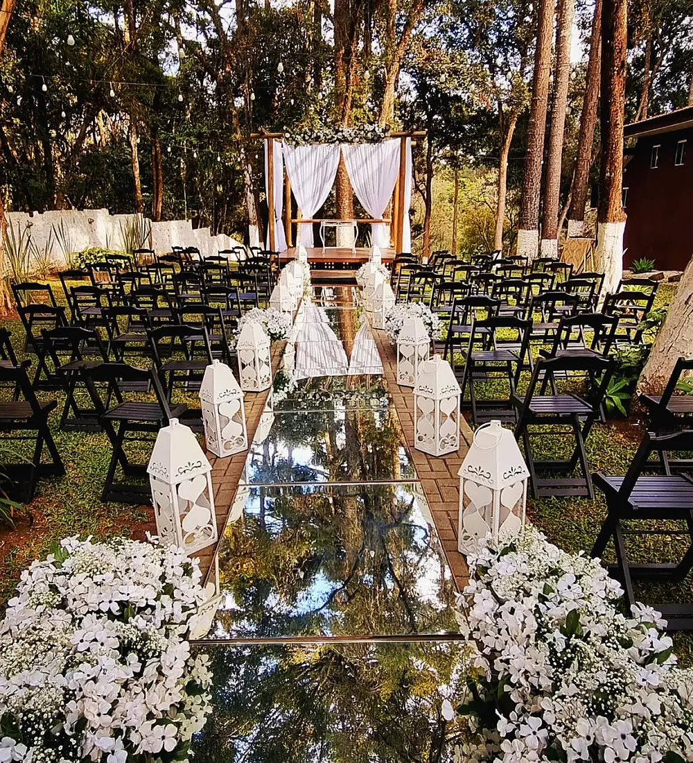 Corredor da cerimônia no bosque, com flores brancas e cadeiras dos dois lados
